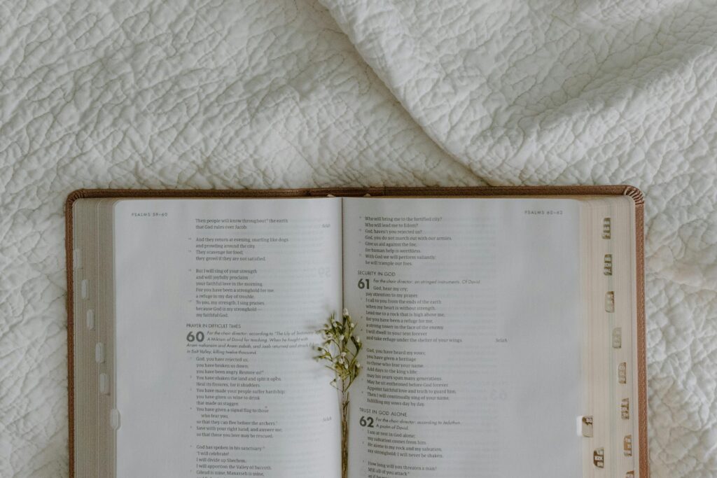 An open Bible on a white quilted fabric background with a small flower arrangement.