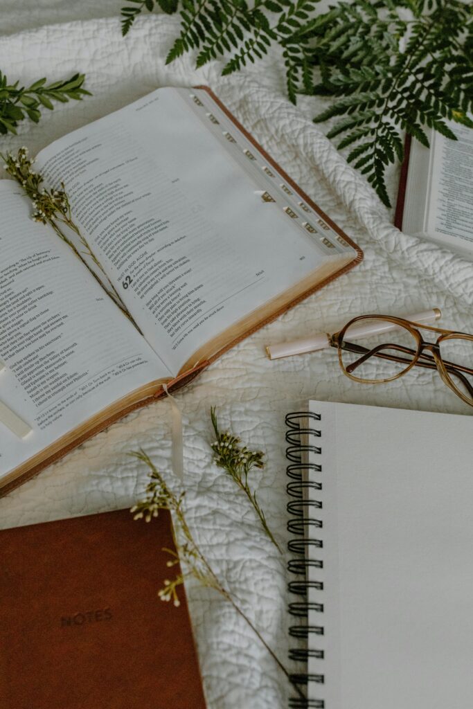 Cozy flat lay of an open Bible, eyeglasses, and notebooks on a white textile backdrop.