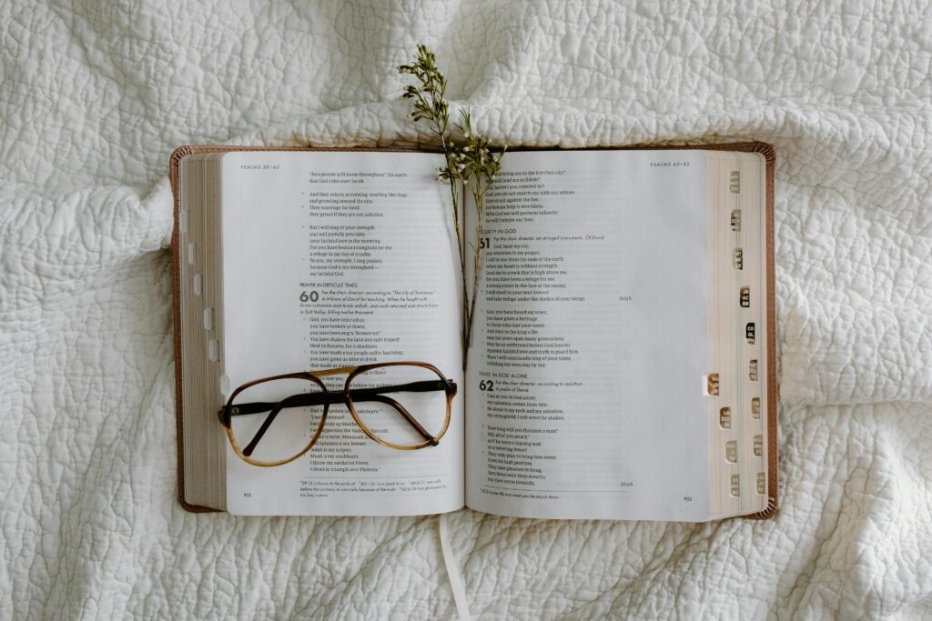 An open Bible with eyeglasses resting on a white quilt, conveying a sense of peace and reflection.